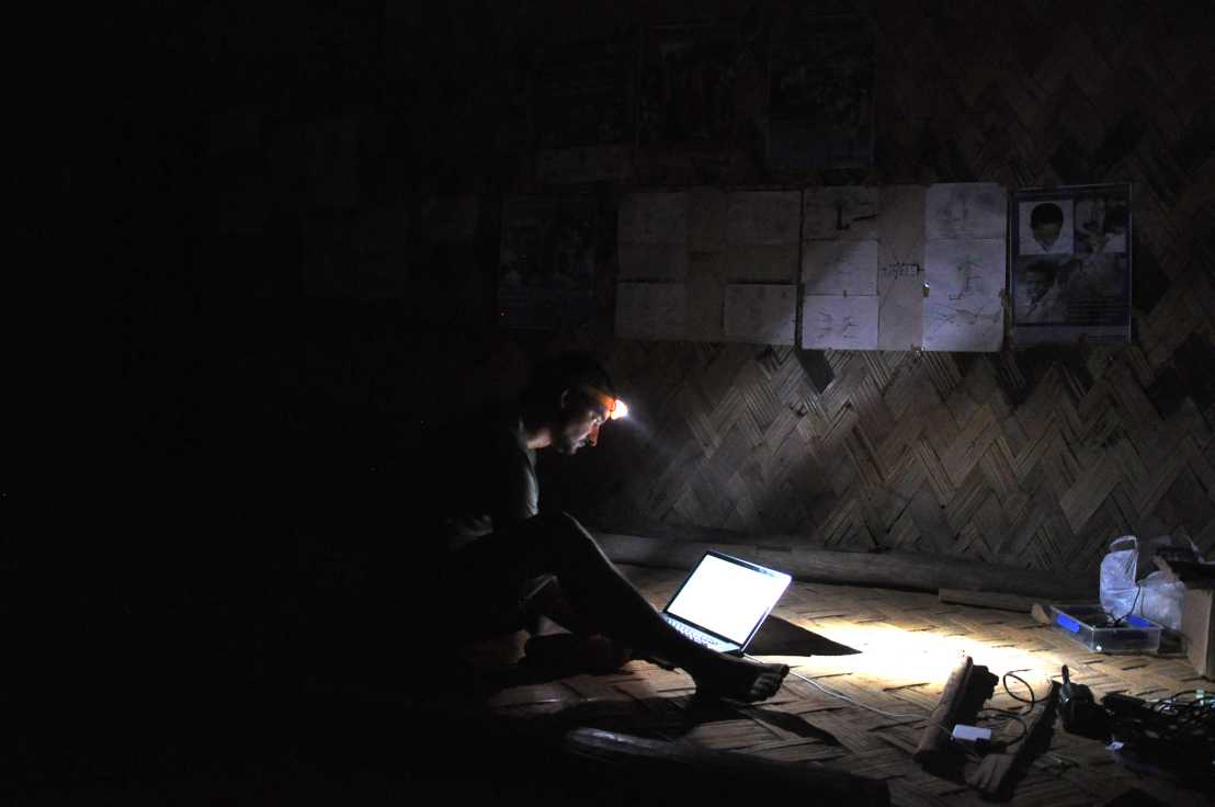 Florian Hanke works on a laptop on the floor in a dark room wearing a head lamp.