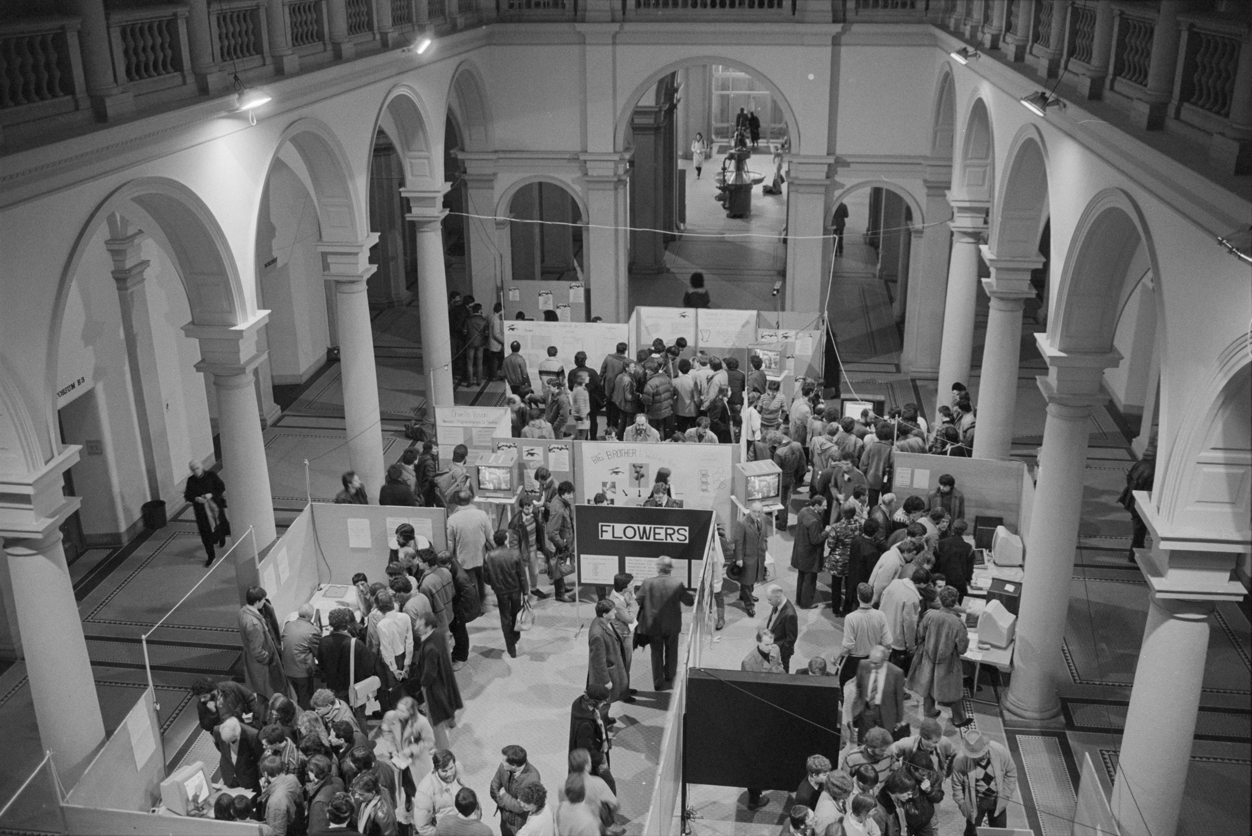 Enlarged view: Black and white photo of the main hall of ETH Zurich's main building, taken from the first-floor gallery. The hall is full of exhibition booths and people in winter clothing.